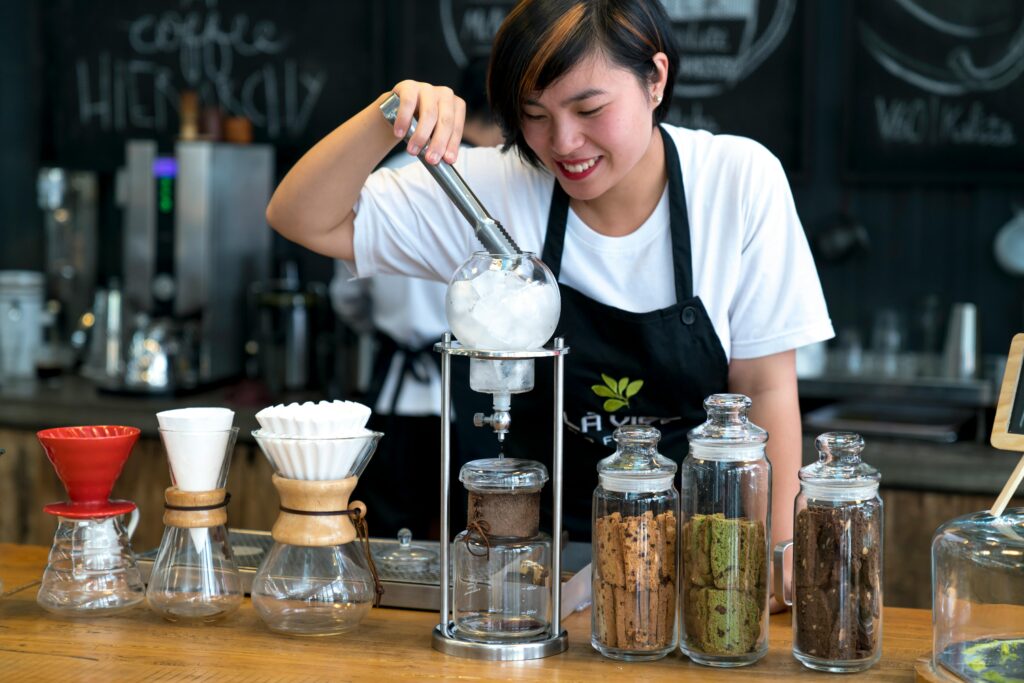 Smiling barista using coffee equipment in a trendy cafe setting.
